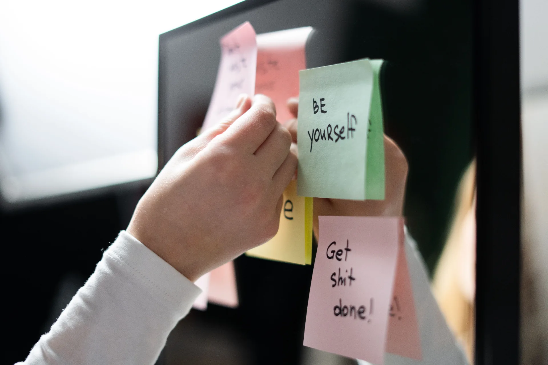 A hand placing a 'be yourself' sticky note
